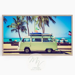 Puede incluir: Una furgoneta vintage blanca con un portaequipajes de techo azul y tablas de surf aparcada en una playa con palmeras y un cielo azul.