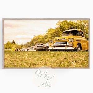 Könnte beinhalten: Ein gelber Vintage-Pickup-Truck, der auf einem Feld geparkt ist, mit anderen Autos im Hintergrund. Der Truck hat eine Chromstoßstange und einen Chromgrill. Das Feld ist mit grünem Gras bedeckt.