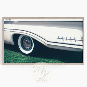 Könnte beinhalten: Nahaufnahme eines weißen Oldtimers mit verchromtem Rad und weißen Reifen. Das Auto steht auf einem Rasen.