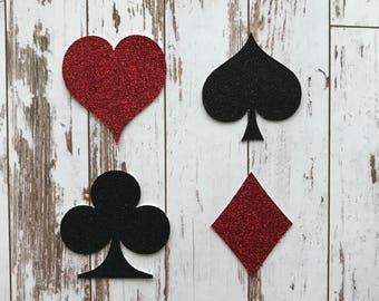 May include: Four red and black glitter card suit shapes: a heart, a spade, a club, and a diamond. The heart and diamond are red, and the spade and club are black.