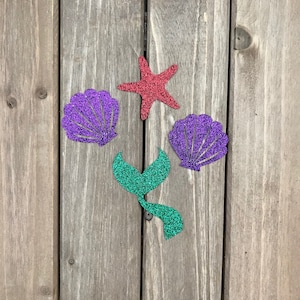 May include: A set of four glitter-covered paper cutouts: a red starfish, two purple seashells, and a green mermaid tail.