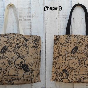 May include: Two tote bags with a brown canvas fabric and black printed postage stamps. The bag on the left has white handles and the bag on the right has black handles.