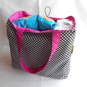May include: A black and white checkered tote bag with pink handles. The bag is filled with snacks and a roll of paper towels.