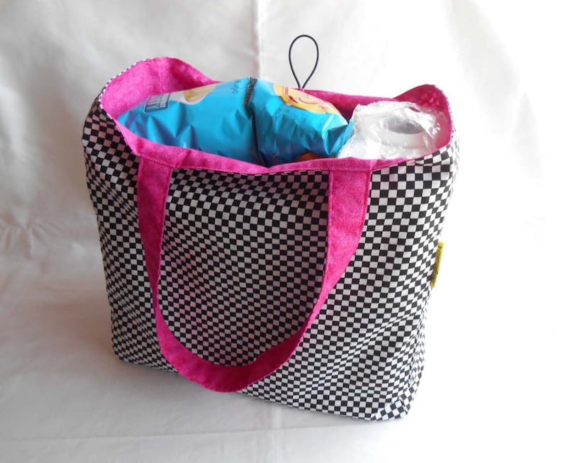 May include: A black and white checkered tote bag with pink handles. The bag is filled with snacks and a roll of paper towels.