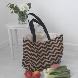 May include: A black and brown chevron patterned tote bag with black handles. The bag is filled with produce, including bok choy and peaches.