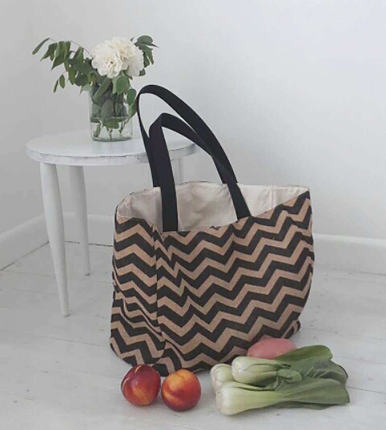 May include: A black and brown chevron patterned tote bag with black handles. The bag is filled with produce, including bok choy and peaches.