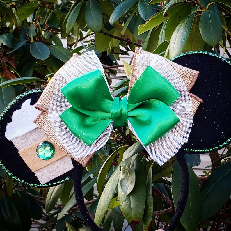 May include: Green and brown bow with a coffee cup design on one side and a black fabric on the other side. The bow is attached to a black headband.