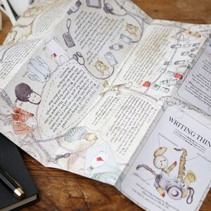 May include: A folded map with illustrations of various objects, including a camera, a stethoscope, a pair of scissors, and a compass. The map is titled "Writing Things" and includes the text "A writing map for the things we love".