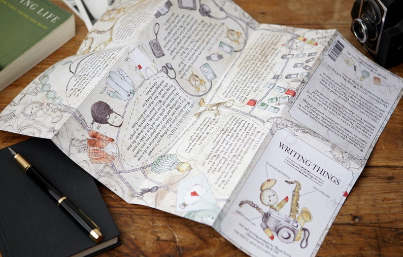 May include: A folded map with illustrations of various objects, including a camera, a stethoscope, a pair of scissors, and a compass. The map is titled "Writing Things" and includes the text "A writing map for the things we love".