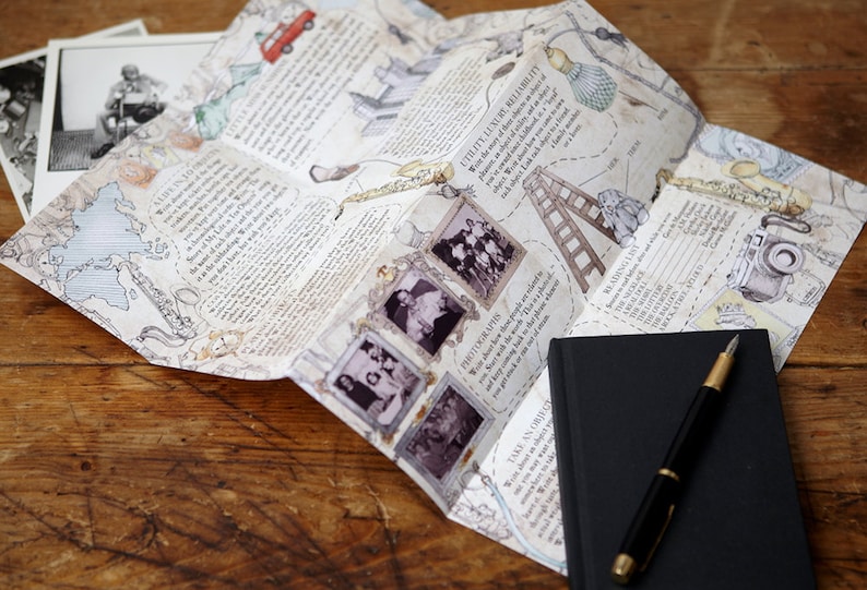 May include: A folded map with illustrations and text about travel and adventure. The map is on a wooden surface with a black notebook and a pen.