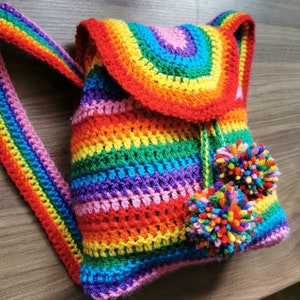 Op de afbeelding: Een kleine regenboogkleurige gehaakte rugzak met twee kleurrijke pompoenen aan de trekkoord.