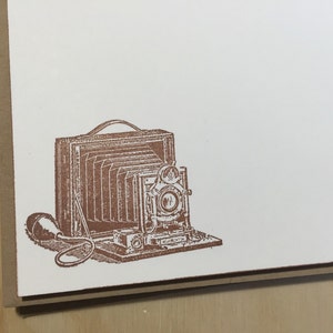 May include: A vintage-style camera with a bellows and a lens. The camera is brown and has a black bellows. The camera is on a white background.