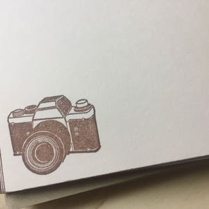 May include: A brown vintage camera with a textured surface. The camera has a round lens and a rectangular body.