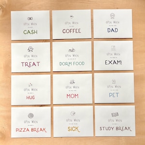 May include: Nine white envelopes with the text "Open When" and various prompts like "Cash," "Coffee," and "Dad." Each envelope has a small illustration and is arranged on a light wooden surface. The prompts are in different colors.