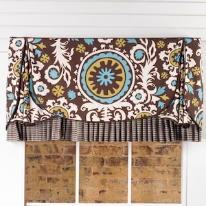 May include: A brown, white, and blue patterned valance with a gingham trim hangs over a window with a view of a brick wall.