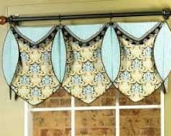 May include: A valance window treatment with three panels featuring a blue and white striped fabric with a scalloped edge and a patterned fabric with a floral design. The valance is trimmed with black and white trim and has a black tassel.