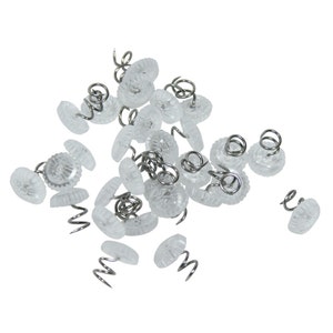 May include: A pile of clear plastic upholstery tacks with silver metal spring coils. The tacks have a decorative, textured top.
