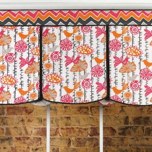 May include: A decorative window valance with a colorful floral and bird pattern. The valance features a white background with orange, pink, and gray floral and bird designs. The top border has a zig-zag pattern in orange, pink, and gray.