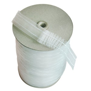 May include: A roll of white, gathered curtain heading tape. The tape is made of a sheer, woven material with vertical lines. The roll is made of cardboard and is cylindrical in shape. The tape is partially unraveled.