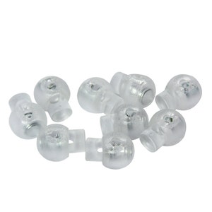 May include: A group of ten clear plastic toggle stoppers with a metal loop. The stoppers are used for securing cords or strings.