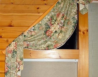 May include: A floral patterned valance with a brown trim hangs over a window with a white blind. The valance is made of a soft, flowing fabric and has a gathered design. The window is set in a wooden frame.