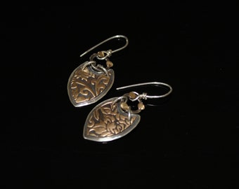 May include: A pair of silver earrings with gold accents. Each earring features a heart-shaped pendant with a floral design.