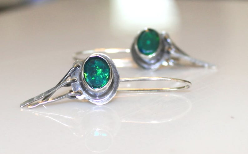 May include: A pair of silver earrings with green gemstone accents. The earrings have a delicate, intricate design.