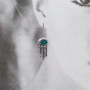 May include: Silver dangle earrings with a green gemstone and a delicate chain design.