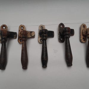 Puede incluir: Cinco cierres de ventana antiguos con manijas de metal negro y bases de metal pintadas de blanco. Las manijas son todas de formas y tamaños ligeramente diferentes.
