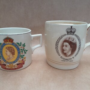 Op de afbeelding: Twee witte keramische mokken met gouden rand. De ene mok heeft een portret van koningin Elizabeth II met de tekst "Elizabeth II June 2nd 1953". De andere mok heeft een koninklijk wapen met de tekst "Dieu et mon droit".