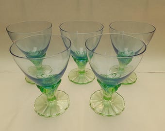 Könnte beinhalten: Fünf Vintage-Stielgläser mit klaren Schalen und grün-blauen Basen. Die Basen haben ein dekoratives, florales Design. Die Gläser sind kreisförmig angeordnet.