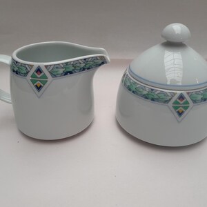 Può includere: Set di brocca per la panna e zuccheriera in porcellana bianca con un design geometrico verde, blu e giallo.