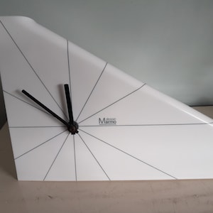 Op de afbeelding: Witte driehoekige klok met zwarte wijzers en een zwart-wit ontwerp. De wijzerplaat van de klok heeft een zwart 'design Marmo' logo.