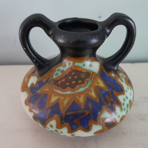 Puede incluir: Un pequeño jarrón de cerámica pintado a mano con dos asas. El jarrón está decorado con un diseño abstracto colorido en tonos de azul, verde, marrón y amarillo.