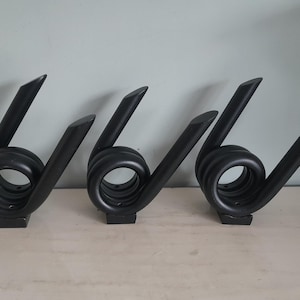 Puede incluir: Tres esculturas decorativas negras con un diseño abstracto. Cada escultura presenta una forma en espiral, similar a un resorte, con una parte superior puntiaguda y una base rectangular. Los objetos están dispuestos sobre una superficie clara.