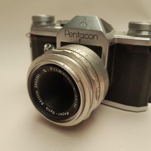 May include: A vintage Pentacon F camera with a silver lens and black leather body. The lens is marked Meyer-Optik Görlitz Primagon 3.5/50. The camera has a silver top with the Pentacon F logo.