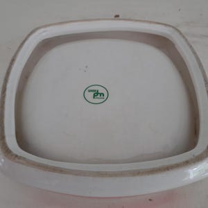 May include: A square, white ceramic plate with a raised, rounded rim. The rim is bordered by a brown band. The plate has a green and white logo that reads "Wade England".