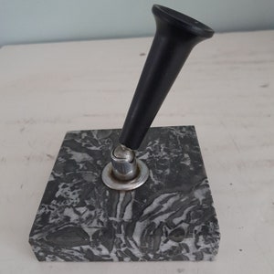 Op de afbeelding: Een zwarte penhouder met een marmeren basis. De penhouder is gemaakt van zwart plastic en heeft een zilveren metalen basis. De marmeren basis is grijs en wit met een draaiende patroon.