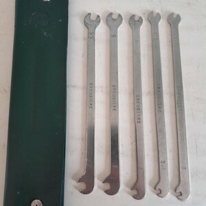 Op de afbeelding: Een set van vijf zilveren sleutels met zwarte handvatten in een groene leren hoes. De sleutels zijn gemarkeerd met "DREIECK" en hebben de maten 3, 3,5, 4, 5 en 5,5.
