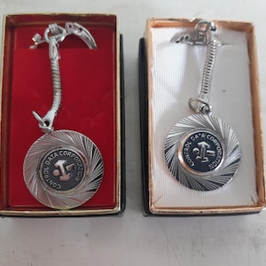 May include: Two vintage silver-toned keychains in their original boxes. Each keychain features a circular pendant with the text "CONTROL DATA CORPORATION" and a stylized logo. The keychains are displayed in red and cream-colored boxes.