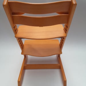 Puede incluir: Silla alta de madera marr&oacute;n claro con respaldo curvo y asiento y reposapi&eacute;s ajustables. La silla tiene una estructura robusta y est&aacute; dise&ntilde;ada para ni&ntilde;os peque&ntilde;os. La silla es de madera maciza y tiene un acabado natural.