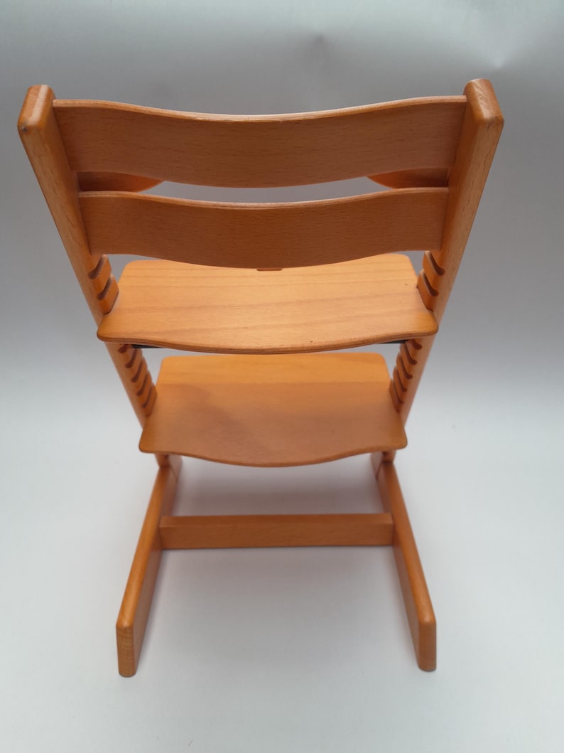 Puede incluir: Silla alta de madera marr&oacute;n claro con respaldo curvo y asiento y reposapi&eacute;s ajustables. La silla tiene una estructura robusta y est&aacute; dise&ntilde;ada para ni&ntilde;os peque&ntilde;os. La silla es de madera maciza y tiene un acabado natural.