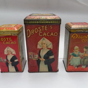 Puede incluir: Tres cajas de hojalata vintage con ilustraciones de mujeres y niños. Las cajas son rojas, amarillas y doradas con el texto "Droste's Cacao" y "Droste's Cocoa".