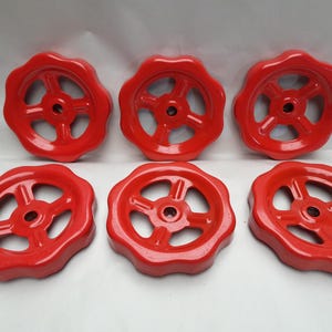 May include: Six bright red valve handles with a circular, spoked design. The handles have a scalloped edge and a central hole for attachment. The handles are made of a solid material and are evenly spaced.