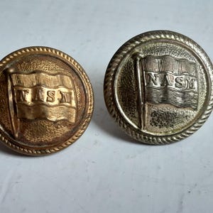 May include: Two vintage metal buttons. One is gold-toned, the other silver-toned. Each button features a flag design with the letters "NASM" on it. The buttons have a rope-like border.