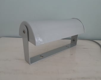 May include: A white metal desk lamp with a curved shade and a simple design. The lamp has a cord and a switch.