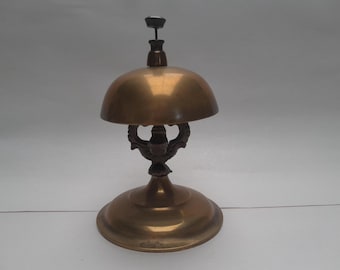 May include: A brass bell with a decorative base and a round top. The bell is used for calling service in a hotel or restaurant.