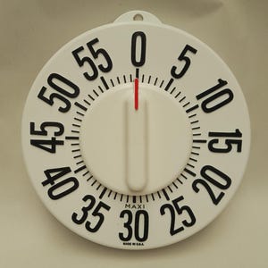 以下が含まれることがあります： 0から55までの数字が黒で表示された白いキッチンタイマー。タイマーには赤いインジケーターと中央に白いノブが付いています。「MAXI」の文字が30の下に印刷され、「MADE IN U.S.A.」がその下に印刷されています。