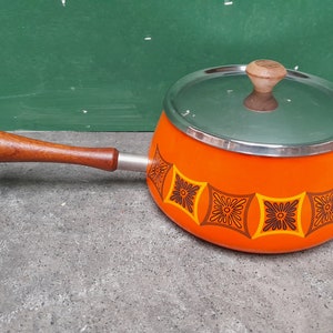 May include: Orange fondue pot with a lid and a wooden handle. The pot has a geometric pattern with brown and orange flowers.