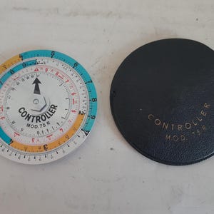 Może przedstawiać: Zabytkowe okrągłe suwmiarki z turkusową, żółtą i białą skalą, z napisem "CONTROLLER MOD.75 R", obok czarnego okrągłego etui z tym samym tekstem w kolorze złotym. Suwak ma centralną strzałkę.